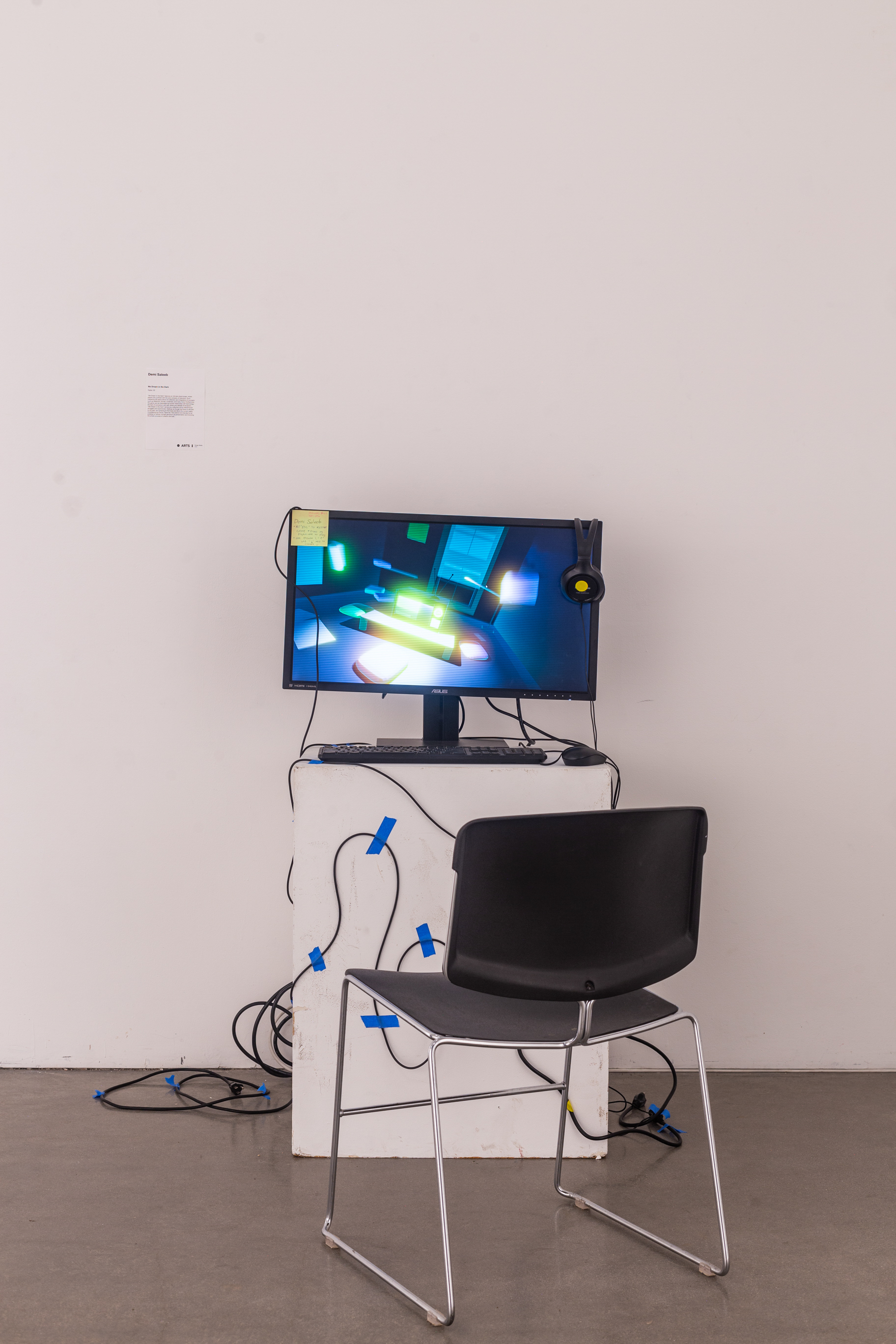 A white podium with a computer monitor, mouse, and keyboard with headphoens on the monitor. On the monitor is an interactive game.